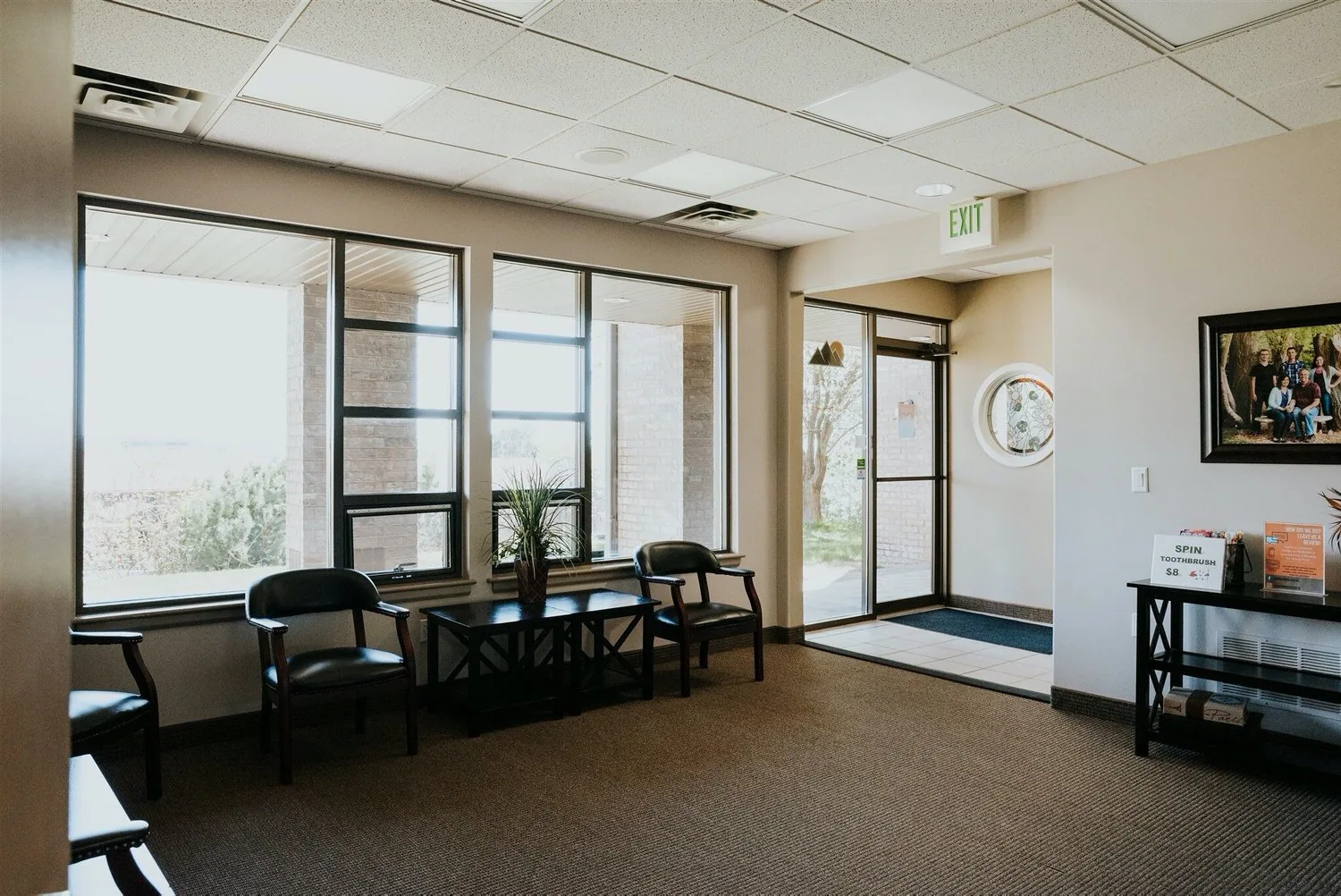 Waiting room with armchairs beside large windows, a potted plant on a table, and a glass entrance door.