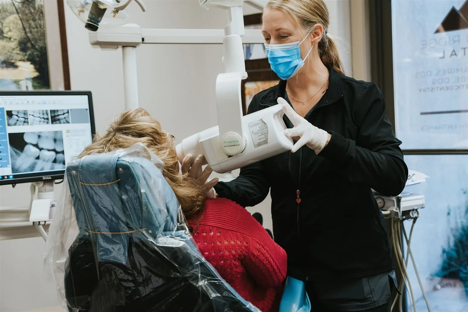 A dental professional positioning an X-ray machine beside a patient seated in a dental chair.