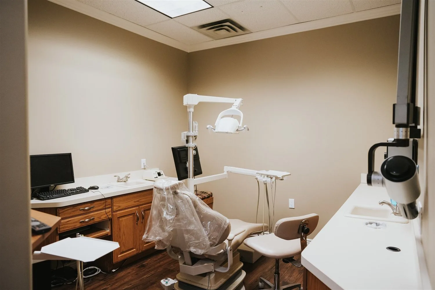 Dental exam room with an examination chair, overhead light, cabinets, and computer workstation.